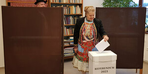 Eine Frau in Tracht wirft einen Stimmzettel in eine Box mit der Aufschrift Referendum 2023