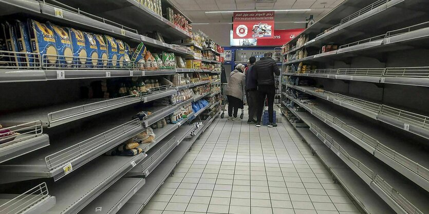 Leere Regale in einem Supermarkt, am Ende der Regale stehen drei Kunden