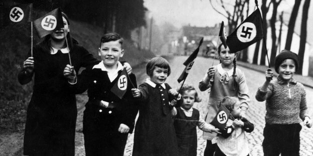 Children walk in the streets and wave swastika flags, laughing