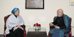 Amina Mohammed im Gespräch mit Hamid Karsai, die beiden sitzen auf roten Samtsesseln, zwischen ihnen ein kleiner Tisch mit Blumenvase