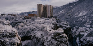 Ein Hochhausbau thront auf einem Felsen in schneebedeckter Berglandschaft