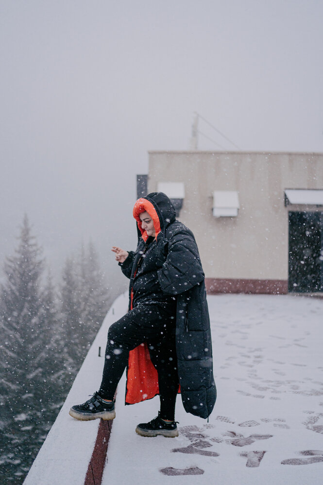 Eine Frau mit schwarzem Mantel und grellem rotem Innenfutter steht im Schnee