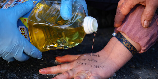 Behandschuhte Hände kippen Öl aus einem Kanister auf eine Hand auf Asphalt.
