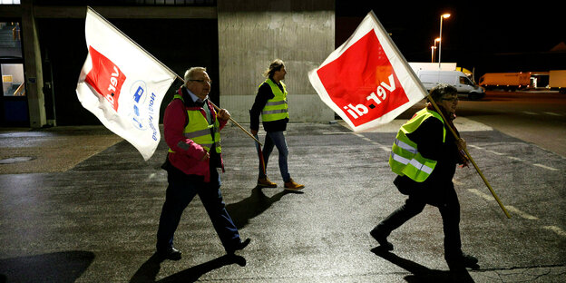 Streikende gehen über das Gelände eines Verteilerzentrums der Post mit Verdi-Fahnen