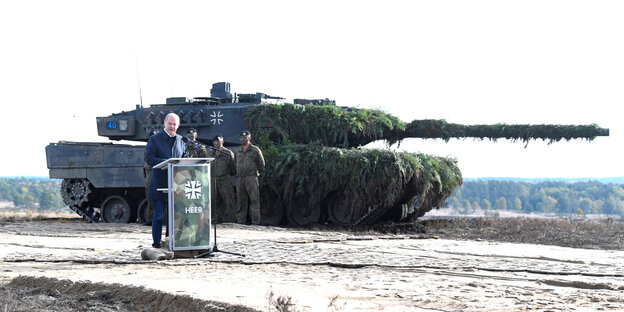Olaf Scholz steht vor einem Leopard 2 Panzer und hält eine Rede vor einem Rednerpult auf dem das Wort "Heer" steht