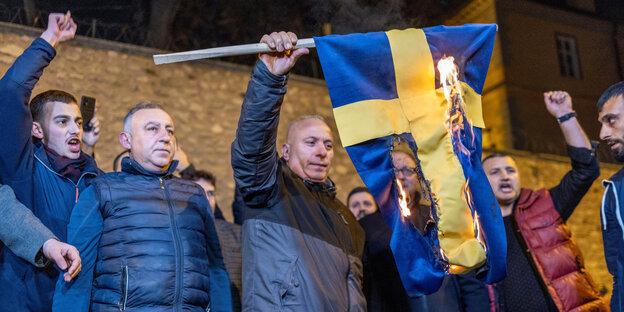 Männer zünden eine schwedische Flagge an
