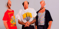 Drei Menschen mit verformten Gesichtern und bunten Klamotten schauen in die Kamera