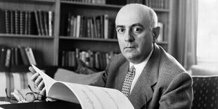 Theodor Adorno sitzt an einem Tisch und hält Noten in der Hand