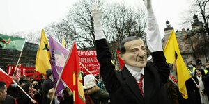 Inmitten einer Protestaktion mit kurdischen Flaggen und roten Transparenten steht eine Erdoganfigur mit weissen Handschuhe reckt die Arme nach oben