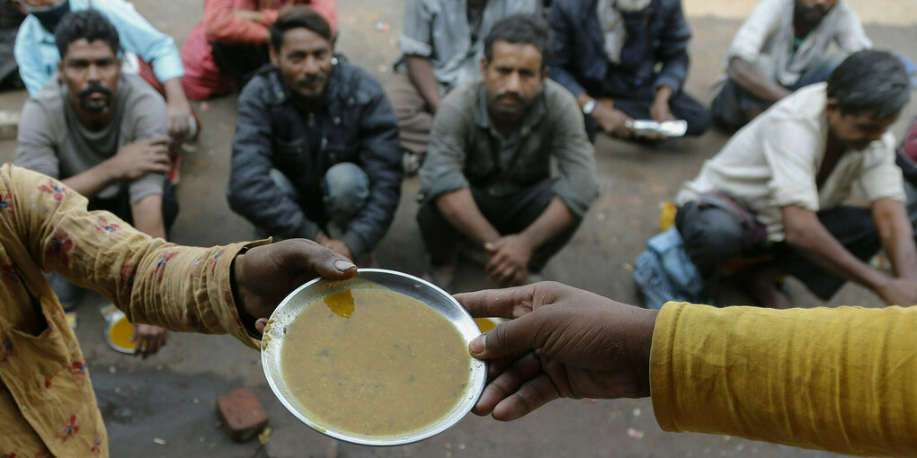 Männer sitzen auf dem Boden und warten darauf, einen Teller Suppe zu bekommen