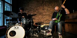 Aufnahme einer Bühne. Rudi Fischerlehner, links im Bild, spielt Schlagzeug, Olaf Rupp, rechts im Bild spielt seine Elektrogitarre