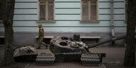 zerstörter Panzer vor einer Hauswand, ein Soldat geht vorbei