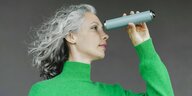 ein Frau mit längeren grauen Haaren trägt einen grünen Pullover und schaut durch Kaleidoskop