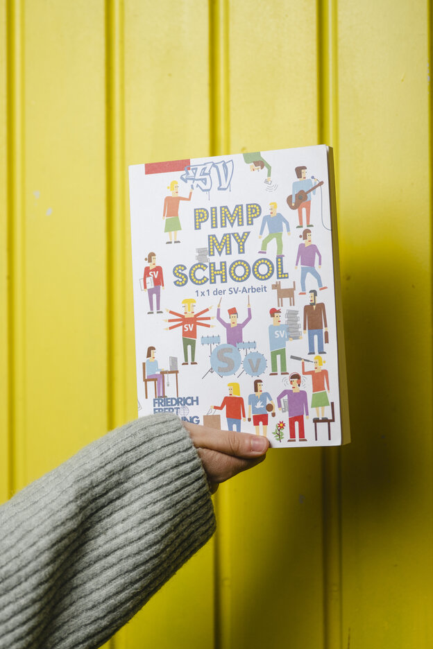 Ein Buch mit dem Titel "Pimp my school" wird hochgehalten