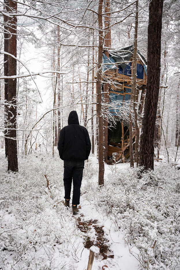 Ein Mann läuft durch einen verschneiten Wald, zwischen den Bäumen ist ein Baumhaus Ein Mann läuft durch einen verschneiten Wald, zwischen den Bäumen ist ein Baumhaus