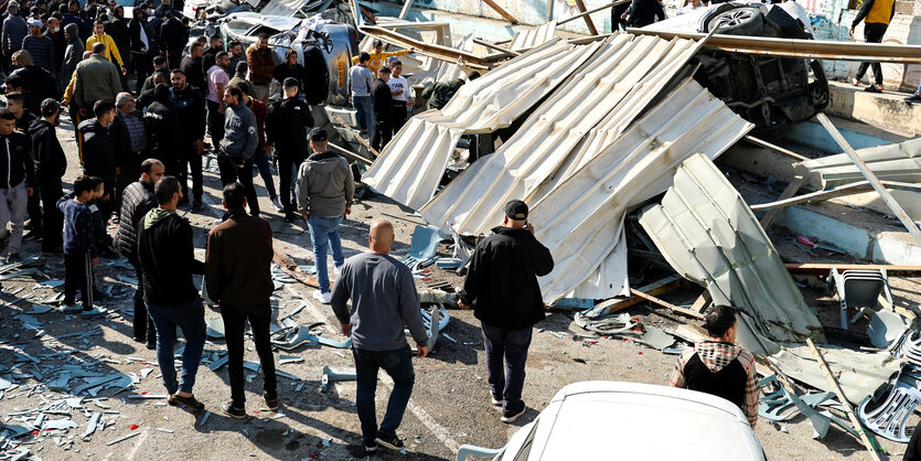 Gruppen von Palästinenser betrachten zwerstörte Autos und Wellbleche, die auf einer Treppe liegen