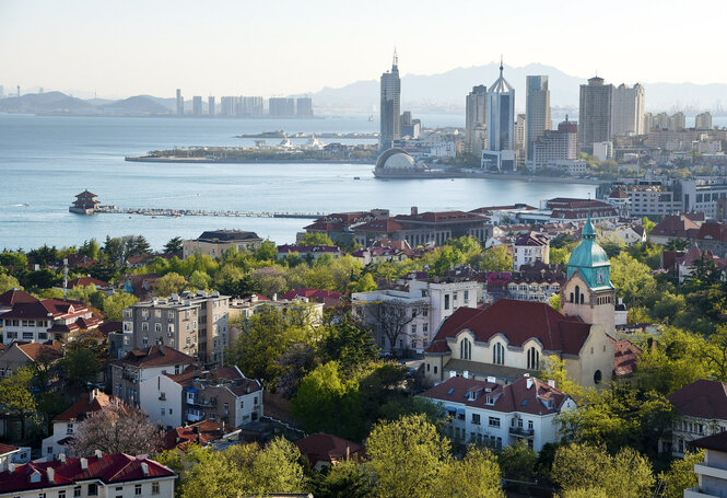 Ein Farbfoto der Hafenstadt Qindao aus dem Jahr 2018. Rote Ziegeldachhäuser sind als architektonische Spuren der deutschen Kololnialgeschichte sichtbar.