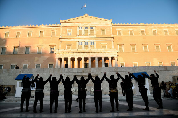 Männer in Trachten stehen mit erhobenen Armen , tänzerisch aneinandergefaßt vor einem Denkmal und dem griechischen Parlament