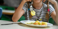 Ein Symbolfoto zum Thema Mittagsessen in Schulmensen zeigt eine halb vollen Teller und ein Kind, dass gerade die Mahlzeit isst