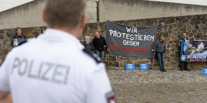 Tierschützer demonstrieren gegen Tierqual, ein Polizist steht davor