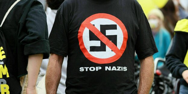 Mann trägt bei einer Demonstration ein T-shirt mit einem durchgestrichenen Hakenkreuz und der Aufschrift: Stop Nazis