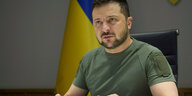 Selenski mit entschlossenem Gesichtsausdruck am Schreibtisch, dahinter die ukrainische Flagge