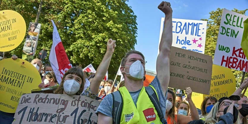 Ein Mann mit Warnweste und eine Frau mit einem Schild recken die Faust in die Höhe bei einer Demonstration