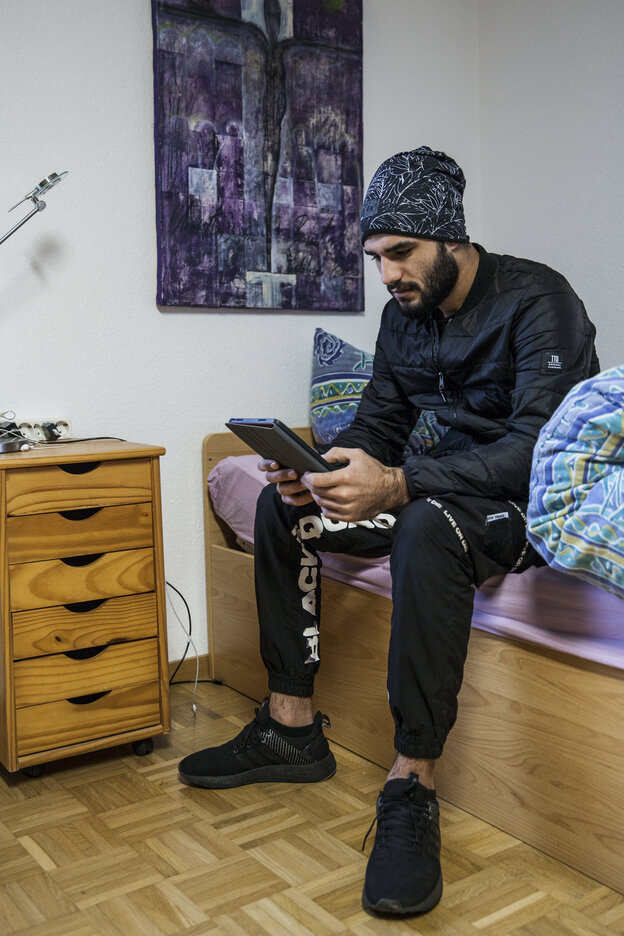 Ein junger Mann sitzt auf einem Bett und schaut auf ein Tablet in seinen Händen