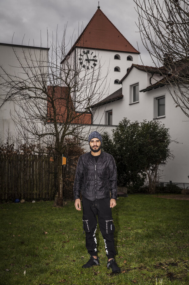 Ein junger Mann mit Kopfbedeckung im Garten, im Hintergrund eine weiße Kirche