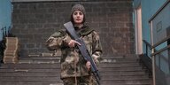 Angin Khachatryan steht allein im Tarnfarbenanzug mit einer Gewehrattrappe in einem Raum