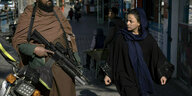 Ein bewaffneter Taliban und eine verschleierte Frau auf einem Gehweg