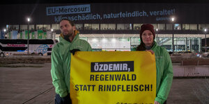 Zwei Aktivisten stehen draußen und halten ein Plakat mit der Aufschrift "klimaschädlich, naturfeindlich, veraltet" in den Händen