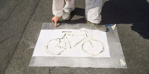 Mensch in weißem Overall sprüht Fahrradsymbol auf Straße