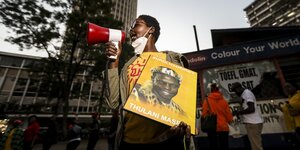 Eine Frau mit Megaphon hält ein Plakat mit dem Portraitbild Thulani Masekos