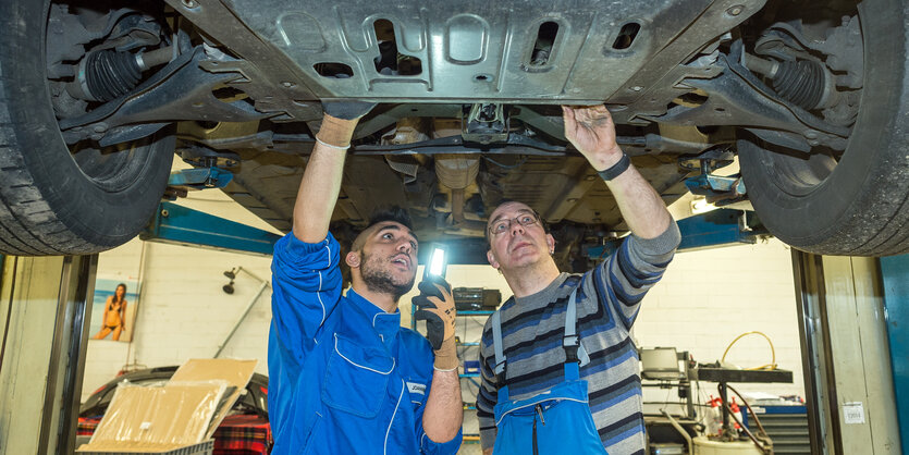 Zwei Menschen in Arbeitskleidung werkeln von unten an einem Auto auf einer Hebebühne