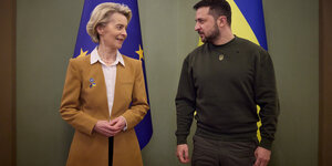 Eine Frau und ein Mann lächeln sich vor der EU- und der Ukraine-Fahne freundlich an