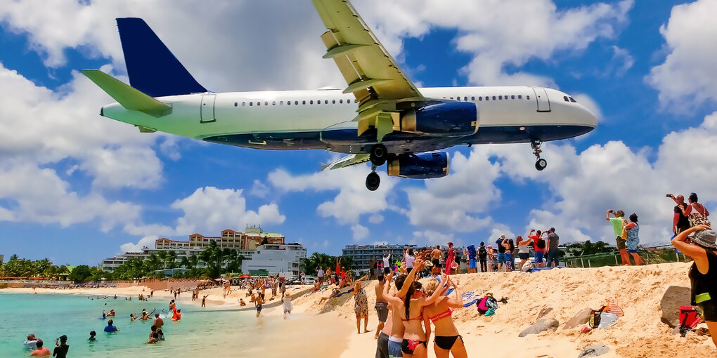 Ein Flugzeug im Landeanflug tief über den Besuchern eines Sandstrandes