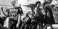 Schwarze und weiße Personen auf einem Platz, einer Trägt ein Shirt mit der Aufschrift " Black Lives Matter"