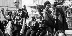 Schwarze und weiße Personen auf einem Platz, einer Trägt ein Shirt mit der Aufschrift " Black Lives Matter"