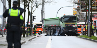 Ein Polizist steht vor dem grünen LKW am Unfallort