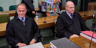 Die Angeklagten Samuel B. und Sebastian T. sitzen vor Gericht und verdecken ihre Gesichter mit Zeitungen und Jacken. Davor sitzen die Anwälte in Anzügen.
