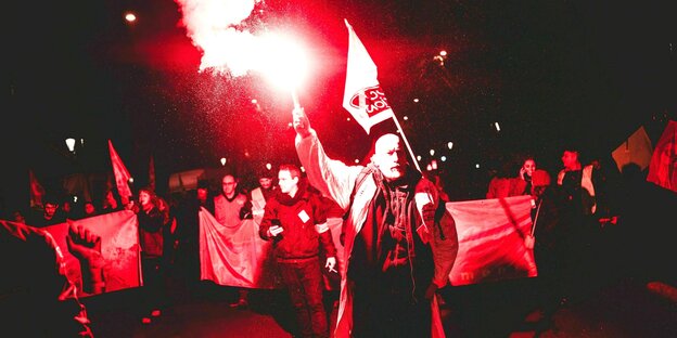 Demonstranten ziehen im roten Licht einer Fackel durch Paris, schwenken Fahnen und tragen Banner
