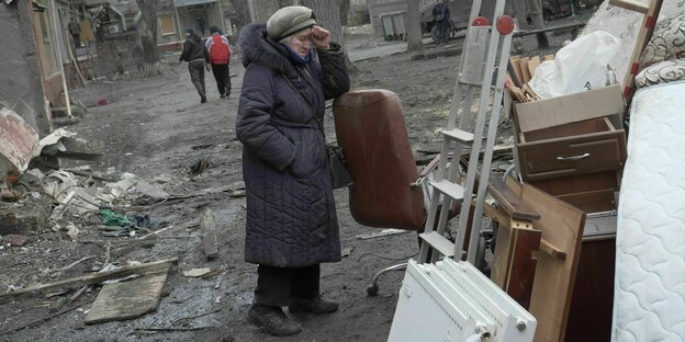 Ältere Frau steht vor ihrem zerstörten Haus
