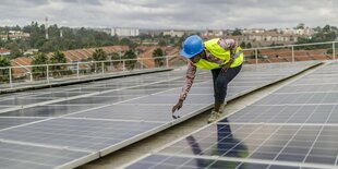 Eine Frau mit Helm steht auf einem Dach das mit Solarpanele ausgestattet ist