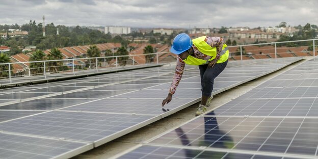 Eine Frau mit Helm steht auf einem Dach das mit Solarpanele ausgestattet ist