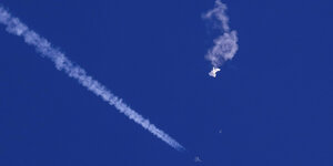 Etwas Rauchendes in der Luft vor blauem Himmel, darunter fliegt ein Kampfjet