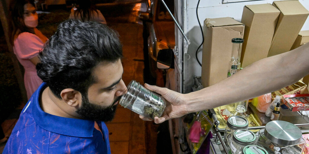 Ein Mann hält die Nase über einem Glas, das ihm entgegengesteckt wird. Er riecht Cannabis