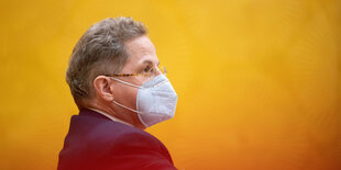 Maaßen mit FFP-2-Maske im Profil fotografiert vor einem orangenen Hintergrund