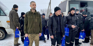 Ukrainische Gefangene stehen vor einem Bus im Schnee und rauchen