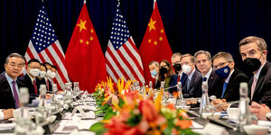 Außenpolitiker an einem Tisch vor US- und China-Flaggen